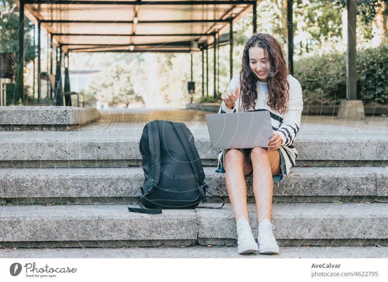 Young arab african student checking his laptop at the university outdoors during a break at the classes, sunset ambient. New studies course, self improvement and learning while reading.