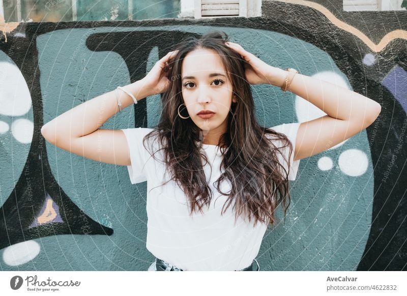 Portrait of a young arab african girl on serious hip hop youngster attitude looking serious to camera on a white shirt with a graffiti background. Beauty young street life street artist at the city