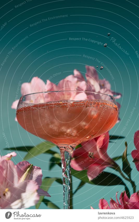 Closeup of wine or cocktail in a glass surrounded by pink and magenta alstroemeria flowers on blue drink beverage alcoholic cold fresh refreshing rosÃ© juicy