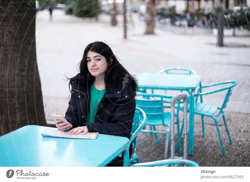 Young woman tourist is sitting in street cafe at table, looking for a way on map, using smartphone. mobile travel young city girl journey female lifestyle