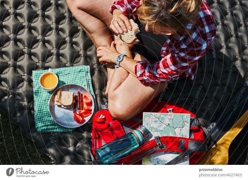 Woman having breakfast sitting by tent at camping. Female actively spending summer vacations close to nature outdoors trip adventure campsite traveling food