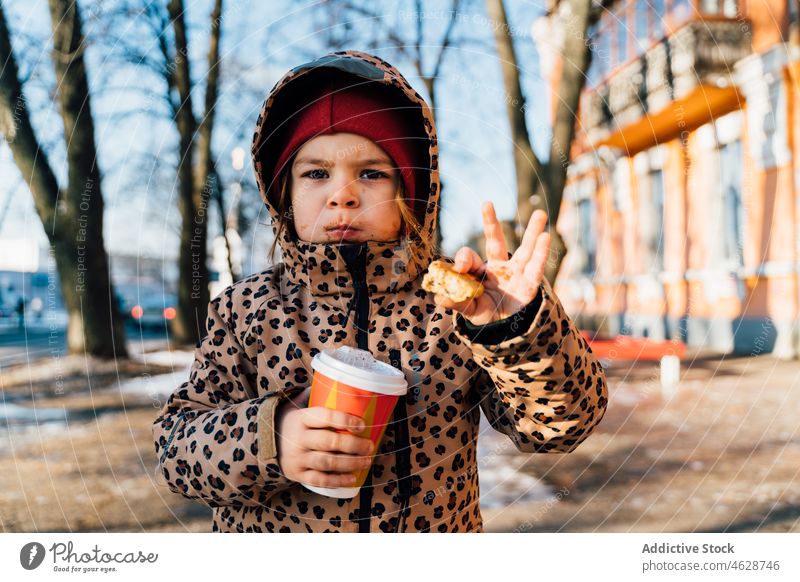 Cute girl with takeaway beverage on winter day kid cookie hot drink street city cold childhood dessert outerwear season snow coffee warm clothes serious