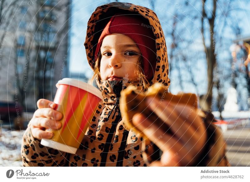 Cute girl with takeaway beverage on winter day kid cookie hot drink street city cold childhood dessert outerwear season snow coffee warm clothes serious