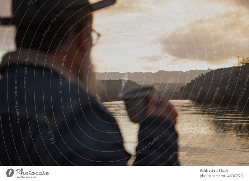 Male traveler drinking coffee on lake shore man beverage hiker sunset forest nature male cup beard sundown warm clothes friend trip trekking friendship guy