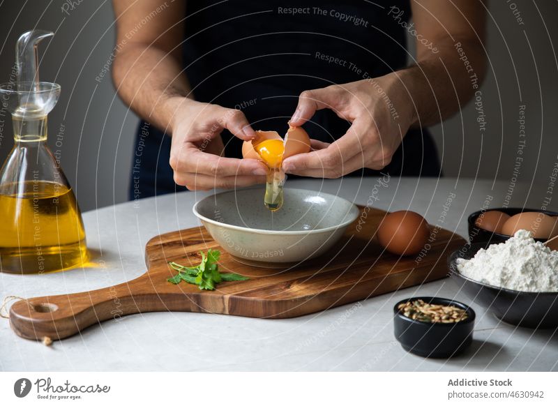 Unrecognizable man breaking egg into bowl cook culinary cuisine recipe ingredient kitchen raw chef prepare food cutting board various product table male add