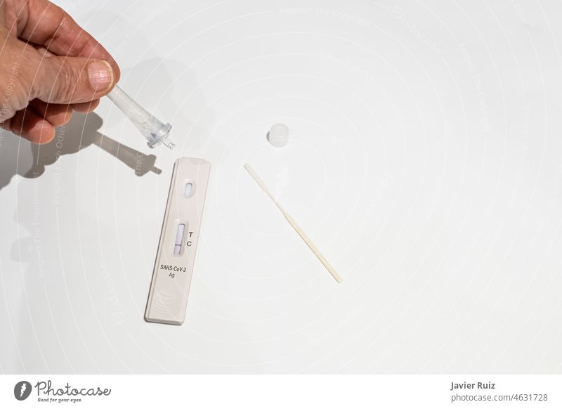 a hand with an eyedropper droplet on an antigen test for corona virus detection, omicron variant, white background, selective focus on the receptor, negative result