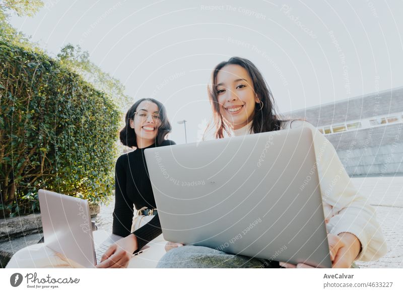 African arab student couple studying outside the campus while working and studying on his laptops, discussing a project to present at class, looking at camera and smiling, back to class concept