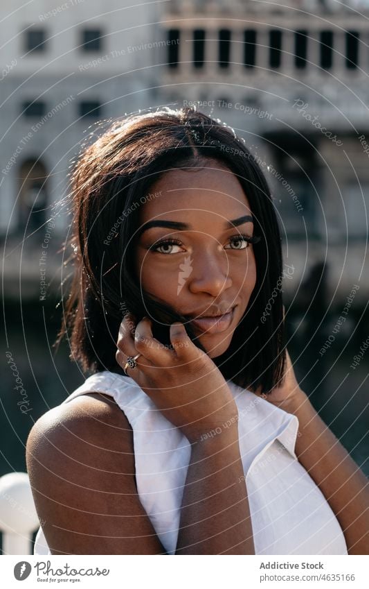 Black woman touching hair while standing on waterfront charming portrait makeup confident feminine individuality gentle cool appearance female embankment