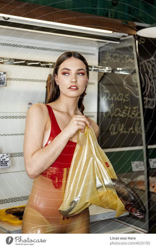 A gorgeous brunette model is posing with a fish in her latex bag. Dressed in a latex catsuit herself she shows some fine fashion looks for everybody in a fish market. Beautiful and fashionable woman in everyday life.