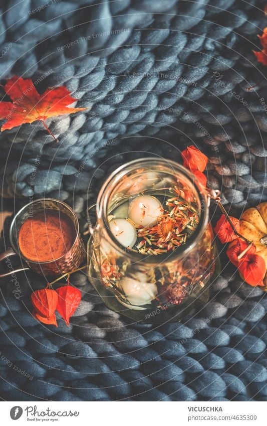 Autumn decoration with water vase and floating candles on grey wool blanket with autumn leaves and coffee knitted cozy indoor fall top view autumn decoration