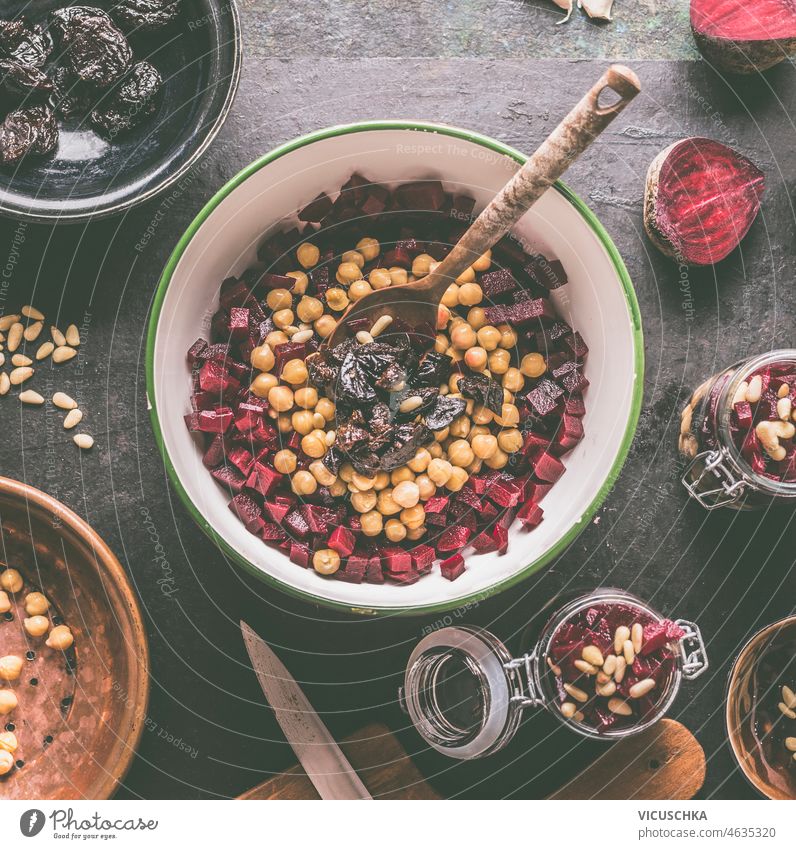 Bowl with beetroot and chickpea salad with dates, garlic and pine nuts, wooden cooking spoon on dark kitchen table. Healthy vegan salad with plant protein and root vegetable. Top view.