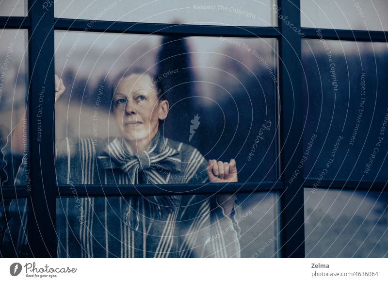 Thoughtful middle-aged woman looks through a dirty window glass thoughtful mature face behind female elderly senior sad sadness alone home bored expression