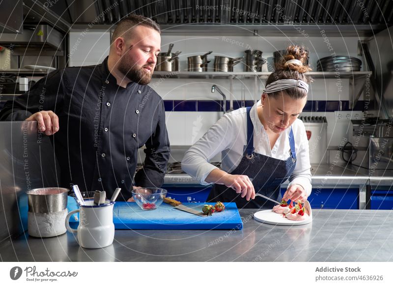 Cheerful chefs cooking dessert together restaurant kitchen colleague collaborate professional man woman bowl crumb cut strawberry work table prepare sweet