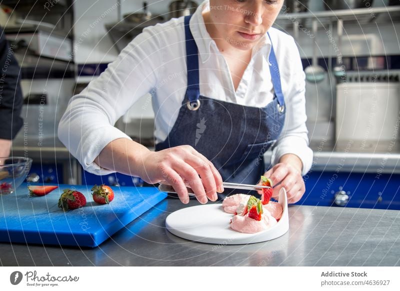 Female cook garnishing dessert with strawberry woman chef cream whipped restaurant kitchen female food prepare apron fresh tweezers add sweet culinary