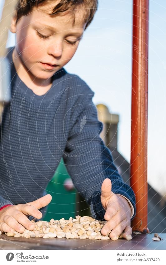 Boy playing with pebbles on playground kid boy childhood amusement playful stone pastime pole metal summer leisure recreation rest cute innocent lifestyle