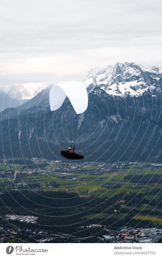 Paraglider flying over village near mountains person paraglider nature settlement range austria salzburg travel extreme ridge adventure flight explore snow high