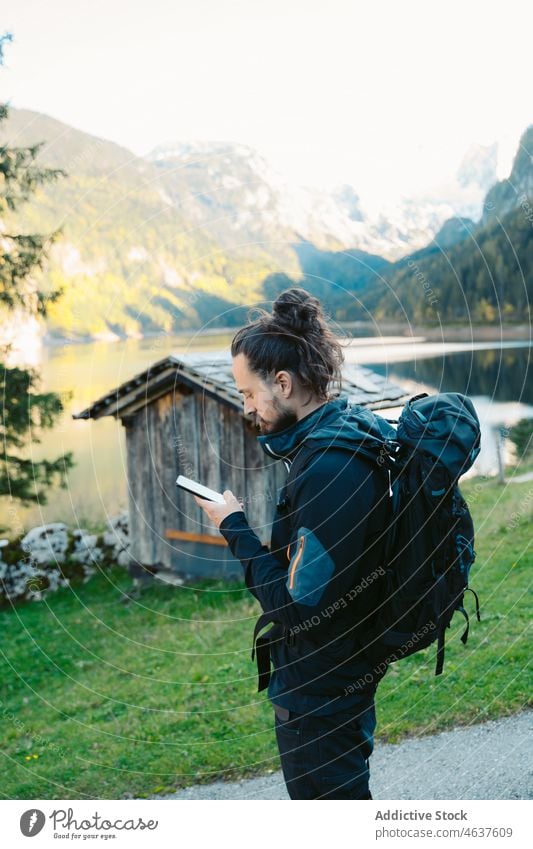 Traveler using smartphone near lake in mountains man nature travel backpacker tourist austria male traveler mobile trip tourism browsing journey internet guy