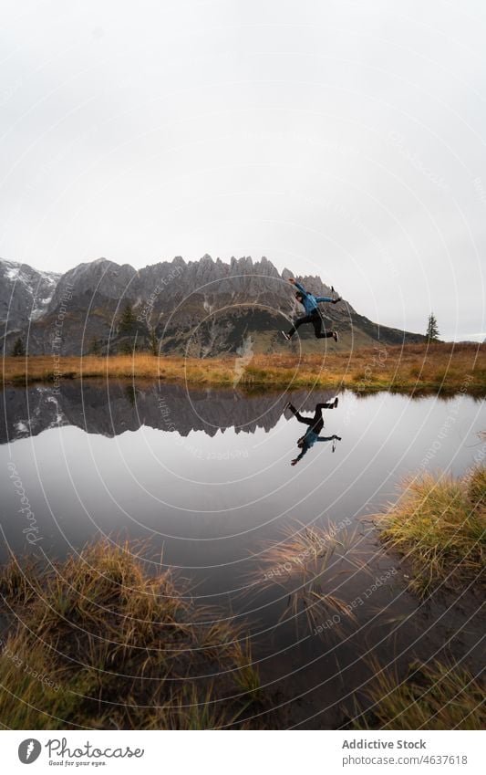 Man jumping near lake and mountains man traveler austria nature landscape range ridge male shore mist tourism reflection calm water countryside freedom guy trip