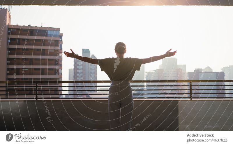 Content young woman enjoying sunny day standing on balcony with outstretched arms cityscape vacation terrace tourist delight happy tourism freedom female casual