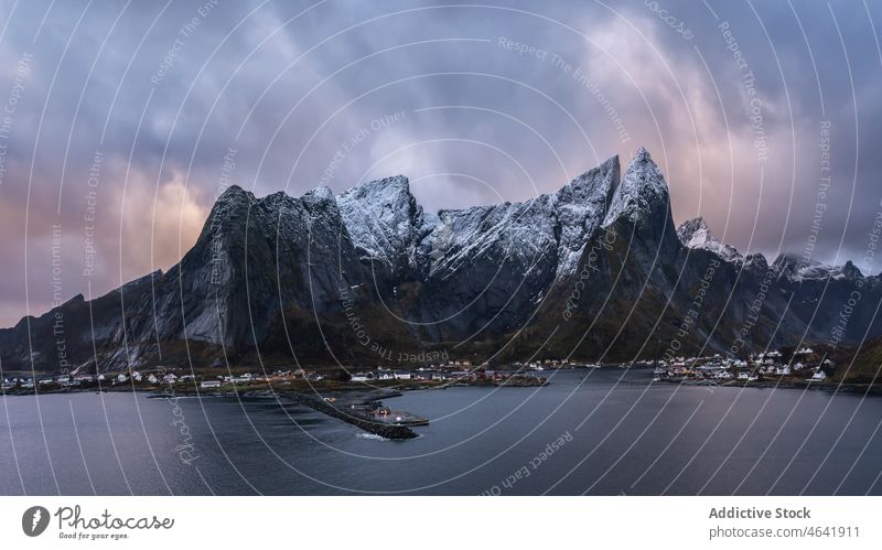 Amazing view of snowy mountains and village located at bottom range settlement house sunset highland landscape picturesque lofoten island norway reine hill