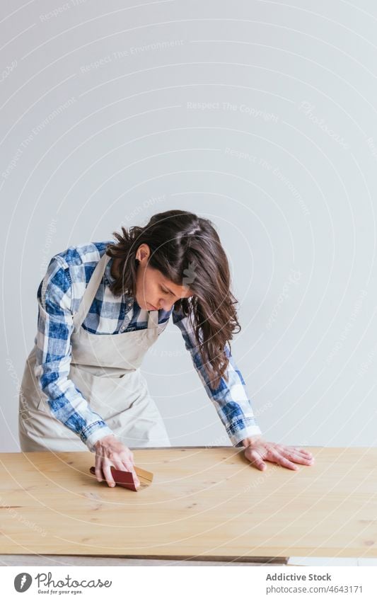 Woman polishing wooden board in workshop woodworker woman sandpaper handwork plank manufacture professional artisan job process occupation apron special timber