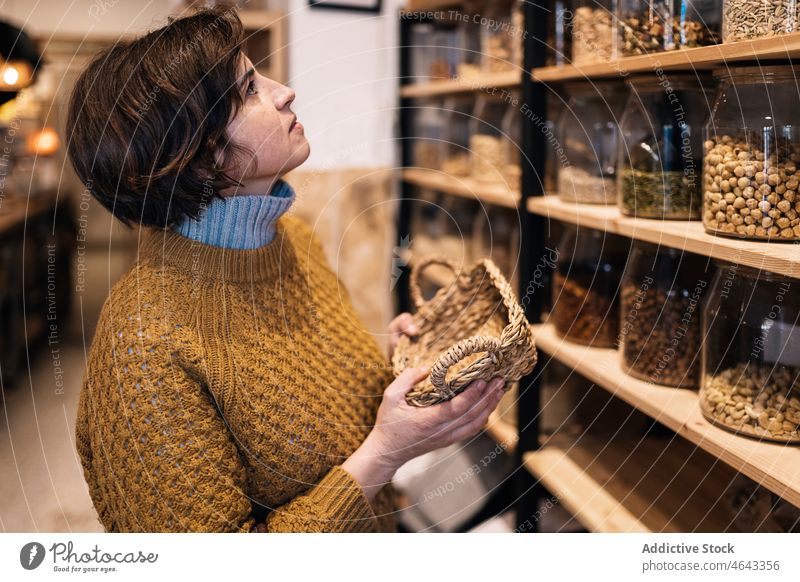 Woman with wicker basket in hands standing in eco store woman eco friendly zero waste shop sweater customer choose female shelf calm natural knitted nut