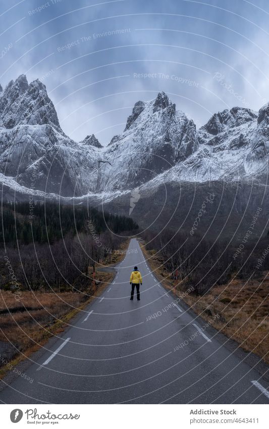 Unrecognizable traveler on road against mountains tourist roadway trip adventure snow winter cliff nature ridge peak empty rock asphalt norway journey vacation