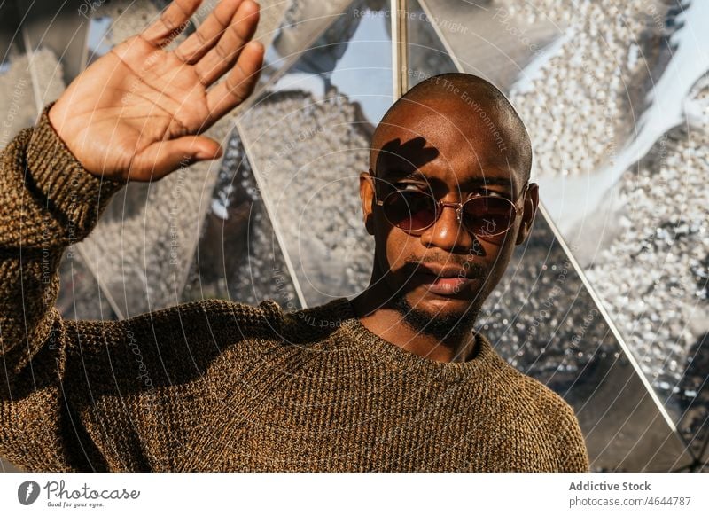 Black man covering from sun with hand sunlight sunny street building appearance style palm sunglasses serious male bald confident trendy african american black