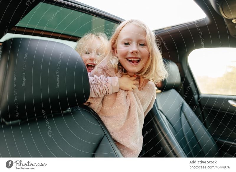 Positive sisters playing in car girl playful having fun road trip pastime passenger automobile commute vehicle journey children transport leisure adventure