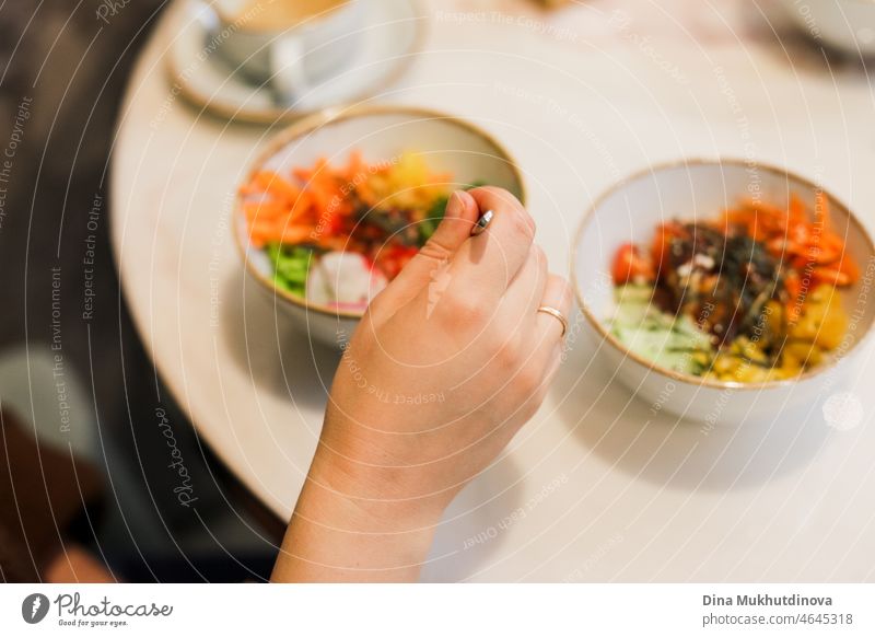 Eating poke bowl at the restaurant. Colorful Hawaiian dish poke bowl made of fresh sliced vegetables ad fish. Hand holding a fork close up. Tasting traditional exotic hawaiian food meal.