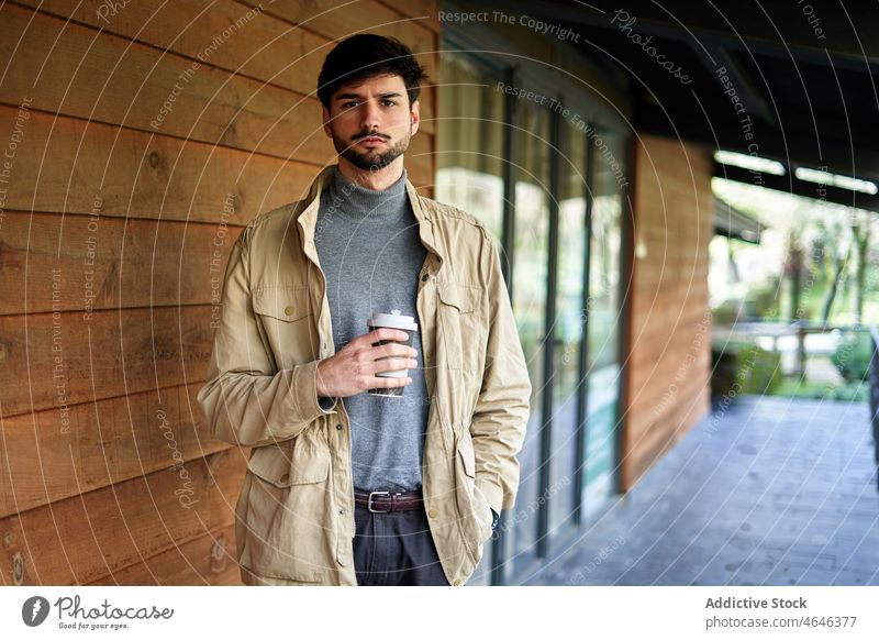 Confident man standing with disposable coffee cup serious takeaway confident gaze thoughtful individuality cool drink male hand in pocket to go street beverage