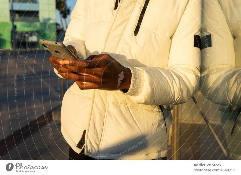 Anonymous African American male browsing phone near glass building wall man smartphone cellphone using texting glass wall reflection black text message city