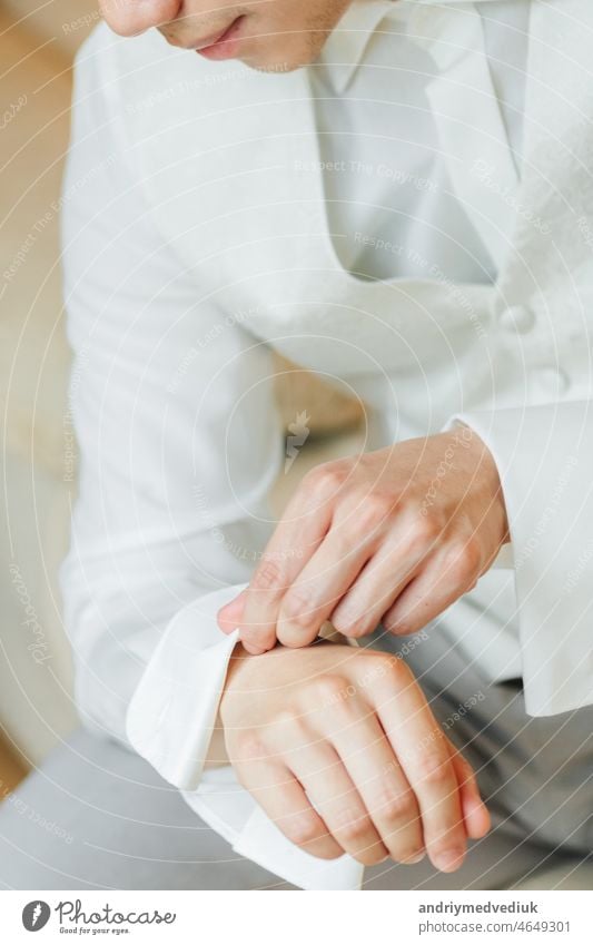 groom in a white tuxedo sitting pinning his shirt brunette man married wedding morning formal clothes hand button celebration suit fashion elegant success