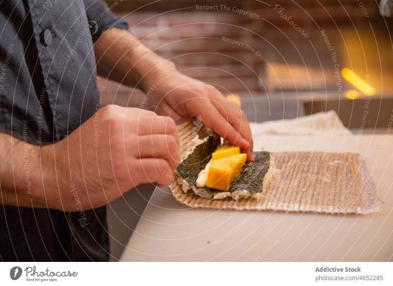 Unrecognizable man rolling sushi with bamboo mat chef radish japanese asian food uramaki cuisine tasty fresh culinary restaurant oriental delicious rice