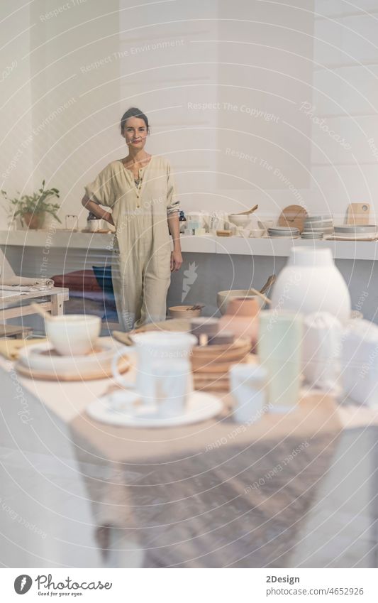 Beautiful happy craft woman wearing apron looking at camera and smiling while standing in her art studio or craft pottery shop workshop ceramist occupation