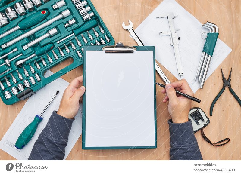 Man working in workshop holding clipboard using many tools. Wrench, spanner, calliper and ratchet with many attachments repair engineering mechanic repairing