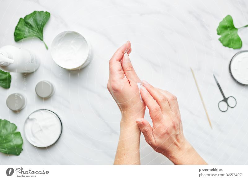 Woman applying  cosmetic moisturizing hand cream. Cosmetic products, green leaves on white table. Spa, manicure, skin care concept nail woman beauty moisturizer