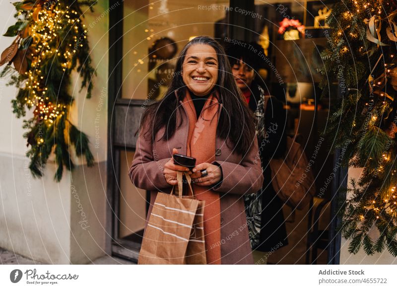 Laughing female clients exiting shop with shopping bags women buyer shopper consume shopaholic city sale cheerful paper bag joy positive purchase optimist store