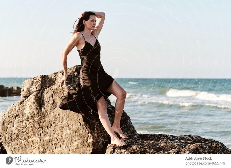 Stylish young female leaning on stone on seashore woman rock dress sensual summer rocky vacation coast water wet recreation formation seaside nature gorgeous