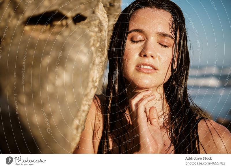 Young woman with wet hair leaning on rocky formation cliff long hair sunlight attractive charming calm portrait appearance nature brunette model individuality