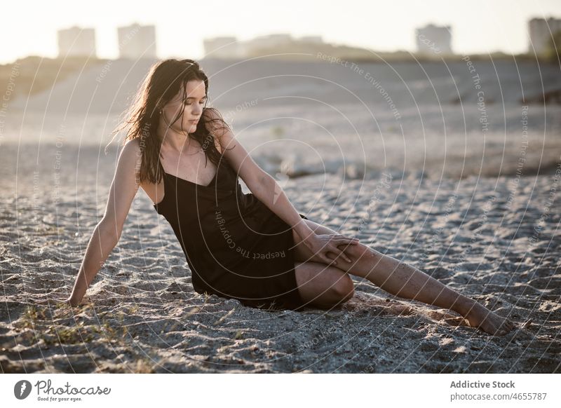 Slim attractive woman sitting on sandy beach in sunny day desert summer cloudless blue sky barefoot dress harmony sundress daytime travel rest relax nature