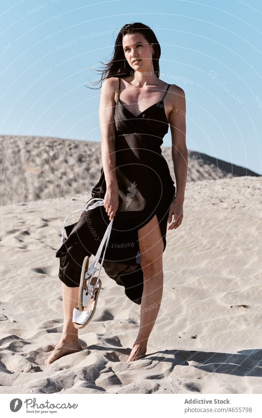 Slim attractive woman standing on sandy beach in sunny day desert summer cloudless blue sky barefoot dress harmony sundress daytime travel rest relax nature