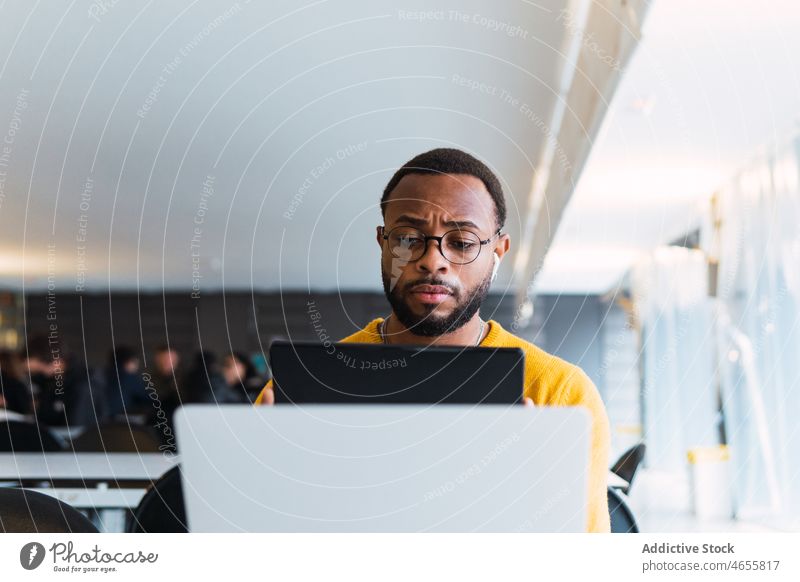 Man with earbuds using tablet and laptop at table man earphones thoughtful listen music workplace meloman serious true wireless male sound audio office gadget