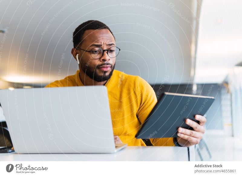 Man with earbuds using tablet and laptop at table man earphones thoughtful listen music workplace meloman serious true wireless male sound audio office gadget