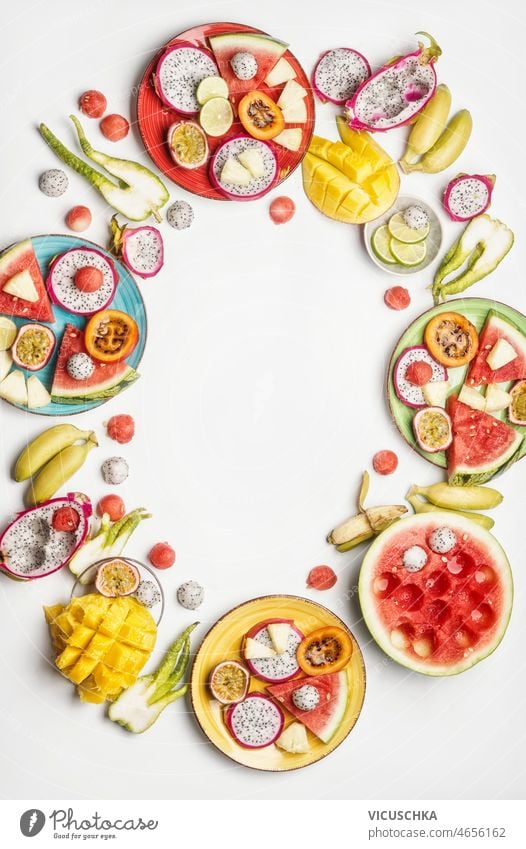 Exotic fruits on colorful plates and white table. exotic fruits circle frame watermelon ananas pitaya banana passion fruits lime mango healthy delicious