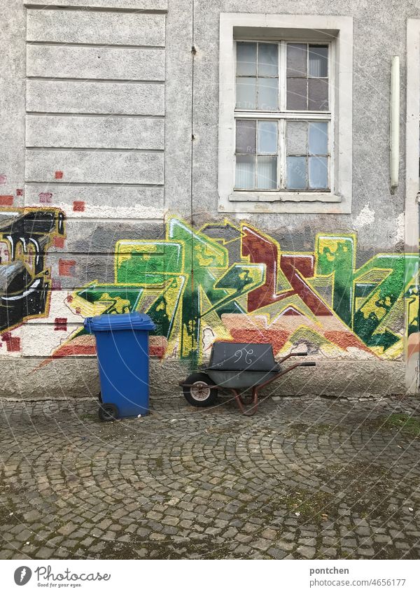 Backyard of an old industrial building with waste paper garbage can and wheelbarrow. Graffiti youth culture Silo Industrial area forsake sb./sth. Shabby