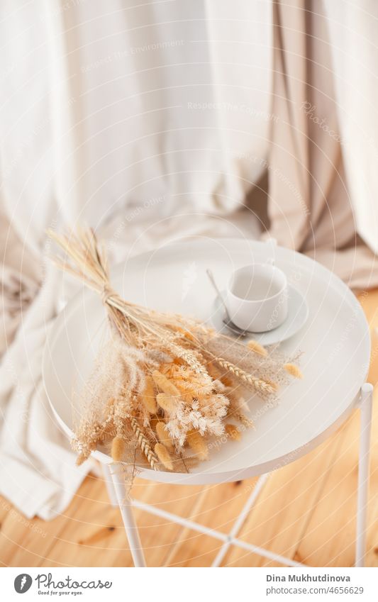 Morning coffee cup with a bouquet of dry flowers and wheat. Breakfast in the morning with coffee and warm sunlight - neutral color lifestyle background with copy space on top.