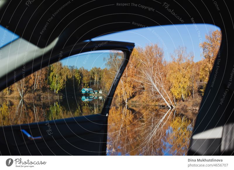 Beautiful peaceful autumn scenery with a house viewed from a window and open door of a car. Fall landscape with a lake on a road trip in autumn. transportation