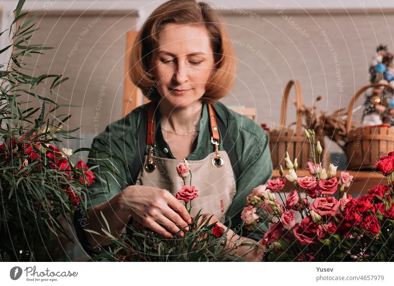 Beautiful woman florist making a gift bouquet of roses. Florist workplace. Small business concept. Front view. Flowers and accessories. Selective focus