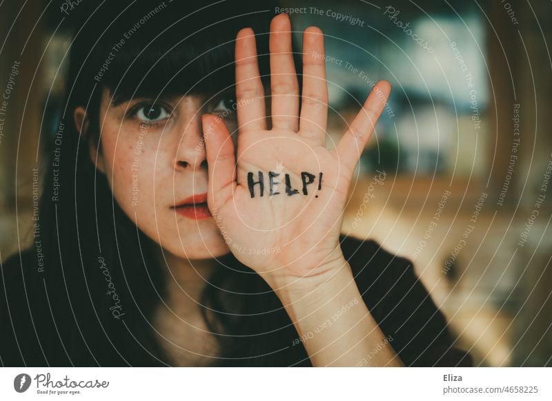 Young woman defensively holds a hand in front of her face on which the word Help is written Woman Protective ask for help Helpless Seeking help